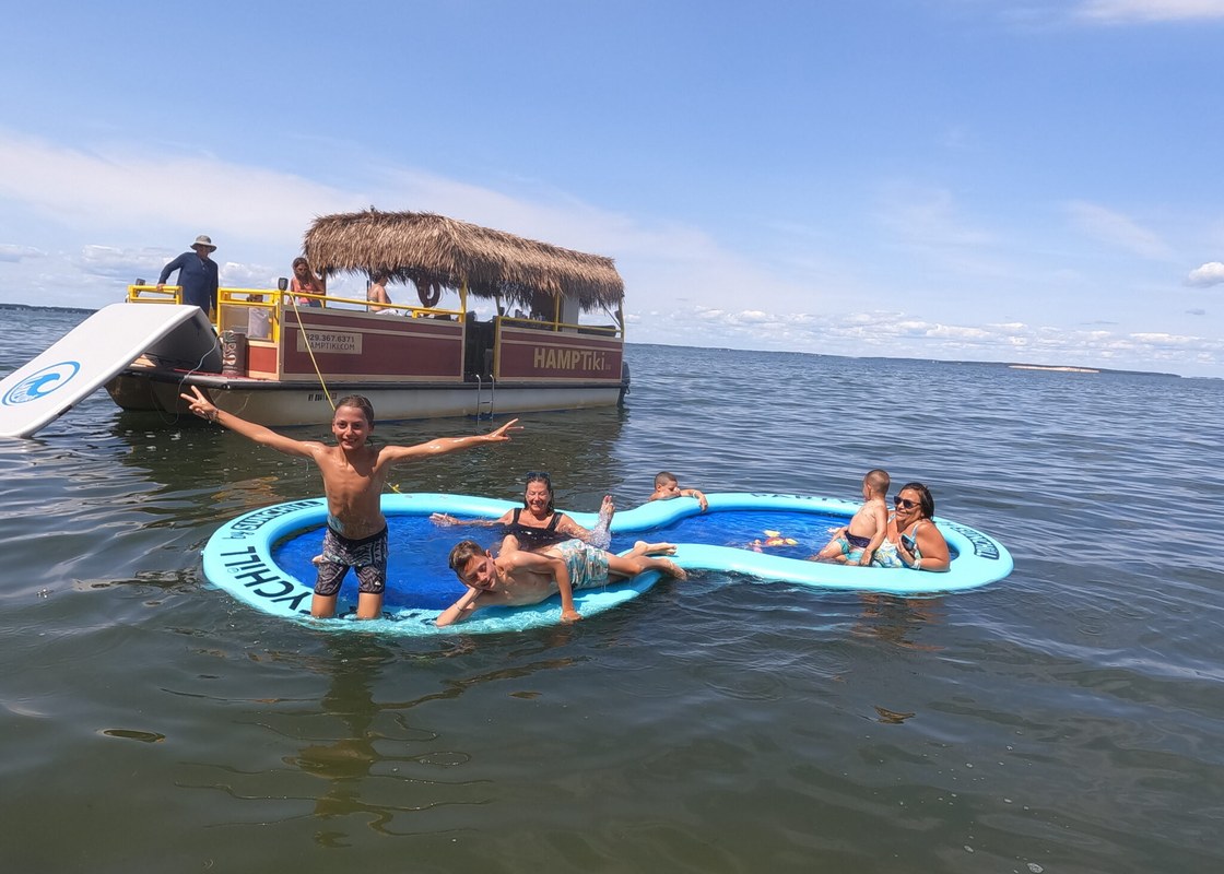 HampTiki tiki boat on Shinnecock Bay with guests relaxing on a floating water mat, Hampton Bays, NY